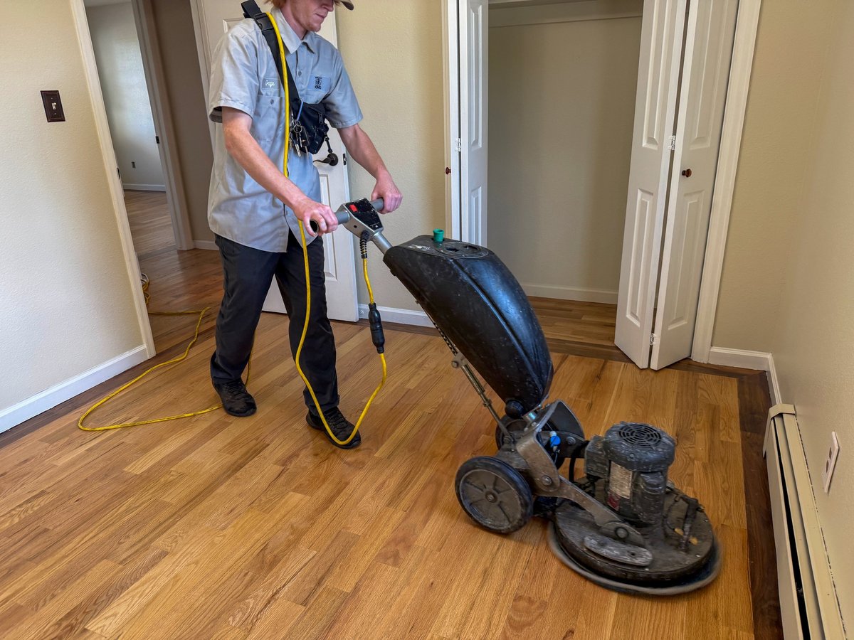 Professional floor technician polishing hardwood floor with industrial buffing machine in residential home