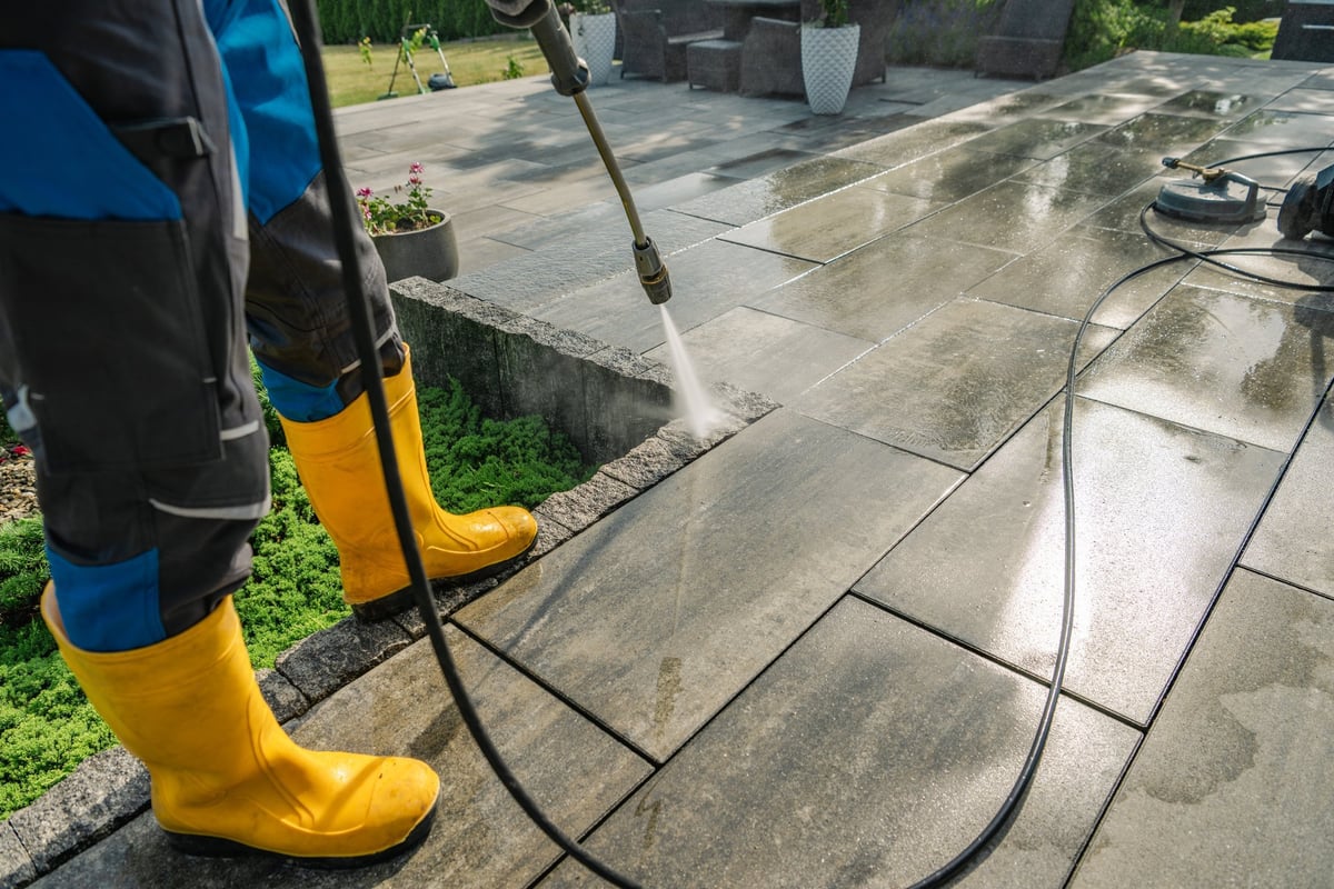 Professional power washing worker cleaning stone patio with pressure washer
