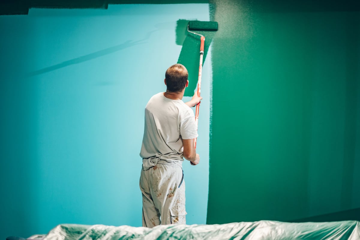 Painter applying paint on a wall, seen from behind during home renovation