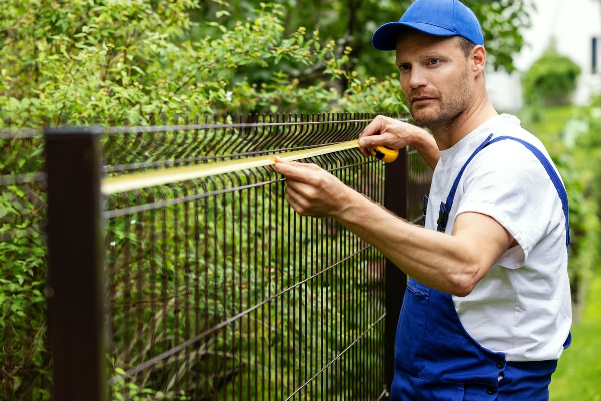 Professional fence installation worker taking measurements for new fence in residential yard