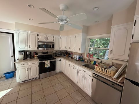 Bright kitchen with white cabinets, stainless steel appliances, tile flooring, and a ceiling fan