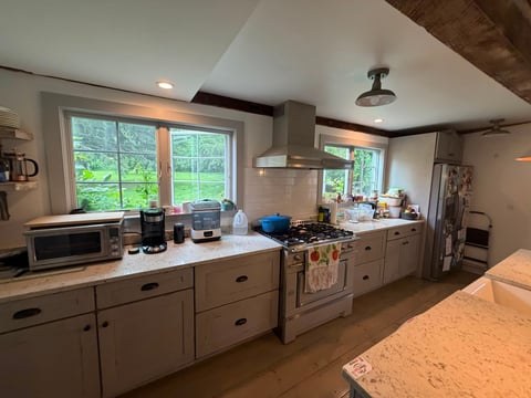 Spacious modern kitchen with white cabinetry, stainless steel stove, stone countertops, and large windows overlooking green landscape