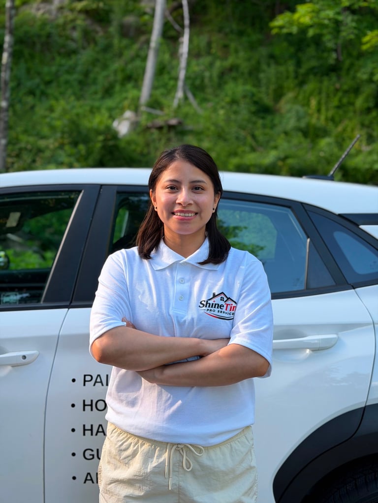 Young woman in light blue polo shirt standing confidently in front of white vehicle with green foliage background