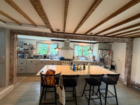 Modern kitchen with exposed wood beam ceiling, large wooden island with black bar stools, and stainless steel appliances.