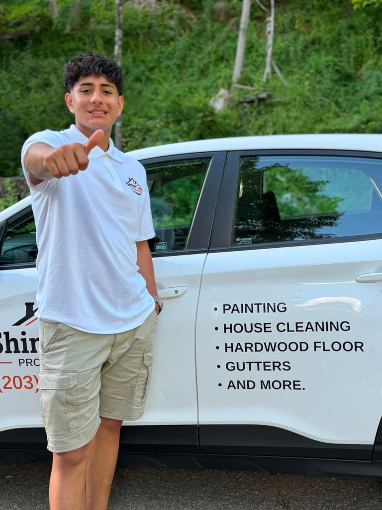 Young man in white polo shirt pointing at camera while leaning against white service vehicle with business services listed on the side