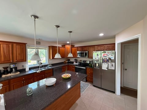Modern kitchen with wood cabinets, dark granite countertops, stainless steel appliances, and pendant lighting over an island