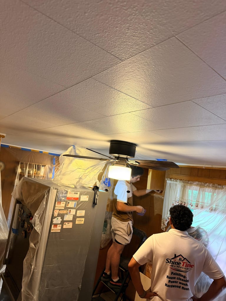 Two workers installing a ceiling fixture in an indoor space with drop ceiling tiles and wooden paneling on walls